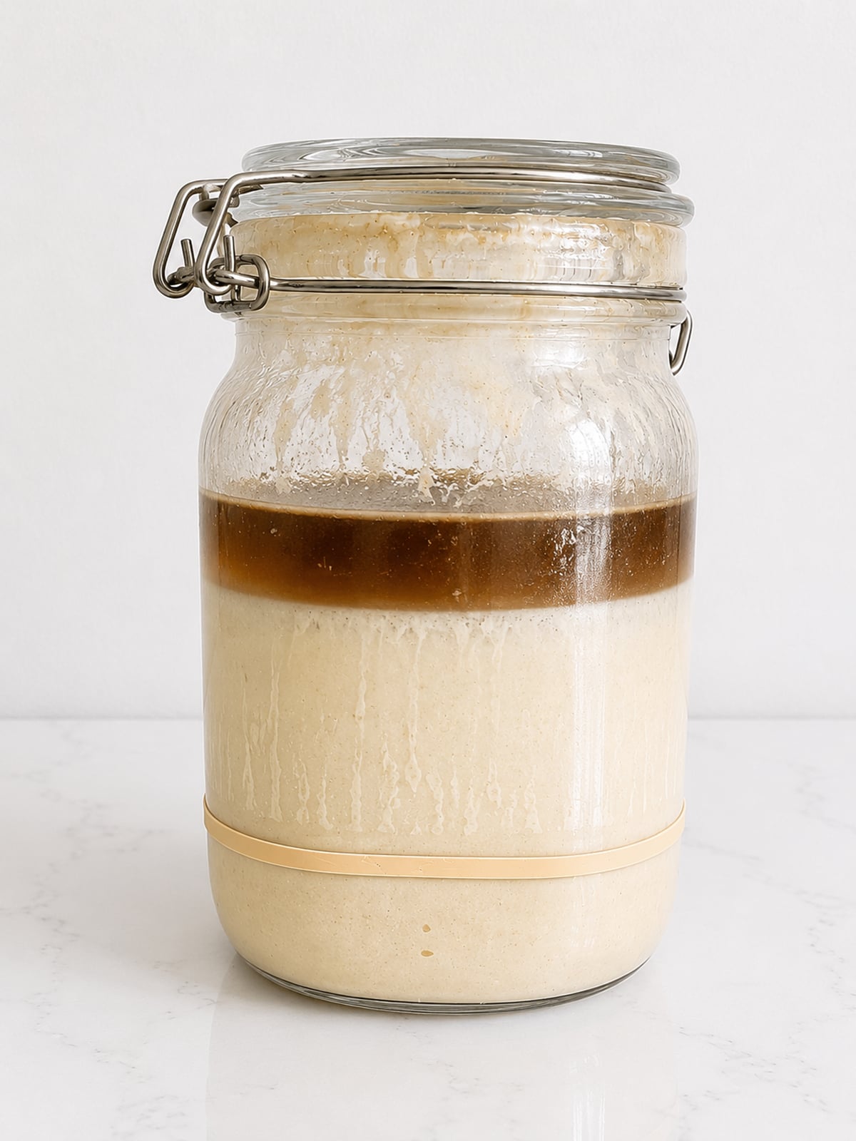Sourdough discard with hooch on the surface in a jar on a white background.