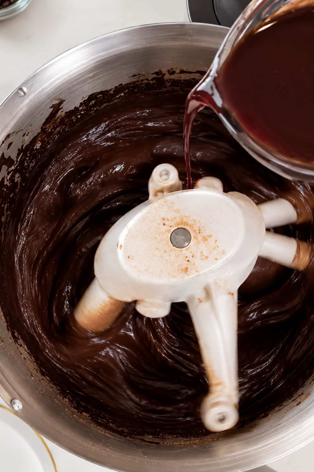 Pouring hot spiced wine into chocolate cake batter in a stand mixer.