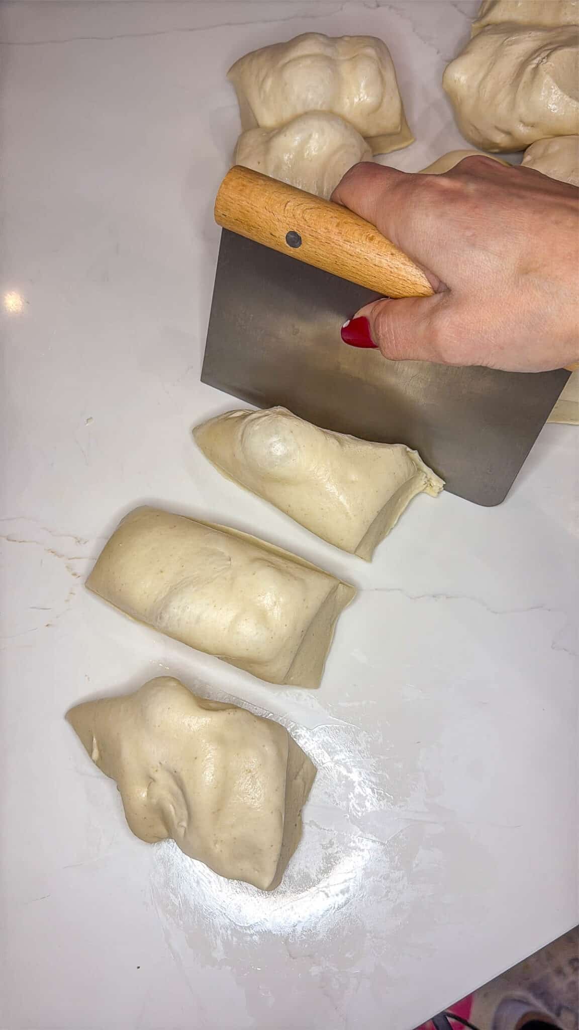 Sourdough discard bagel dough being portioned into pieces with a bench knife.