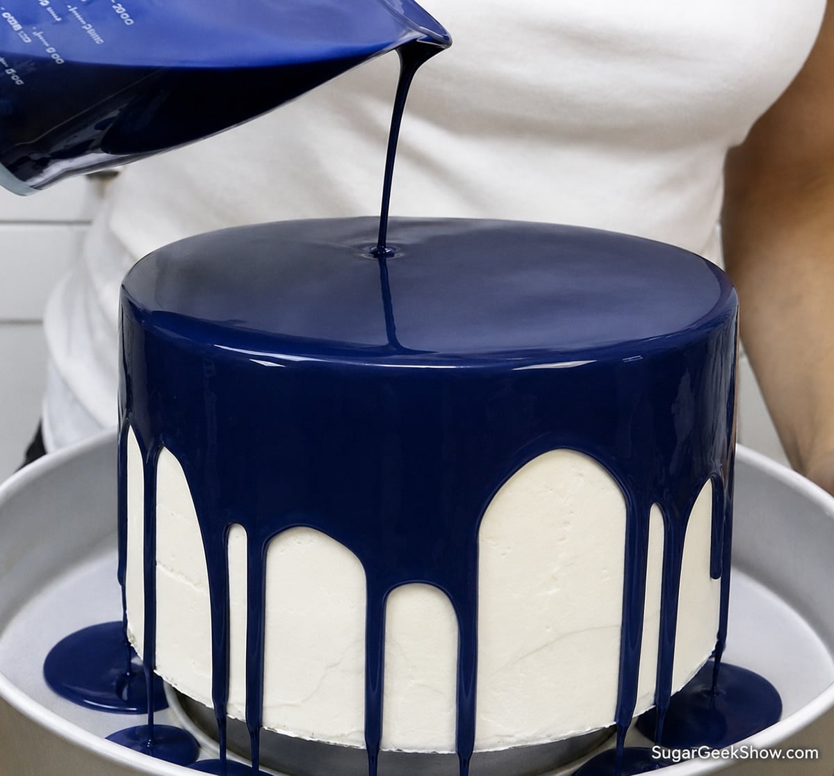 Pouring dark blue glaze over a frozen buttercream cake.