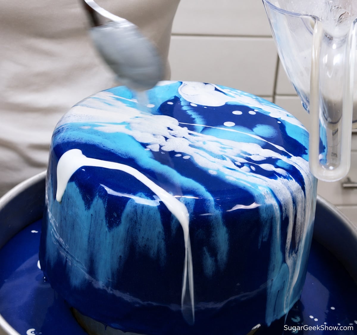 Drizzling light blue and white glaze over a dark blue cake.