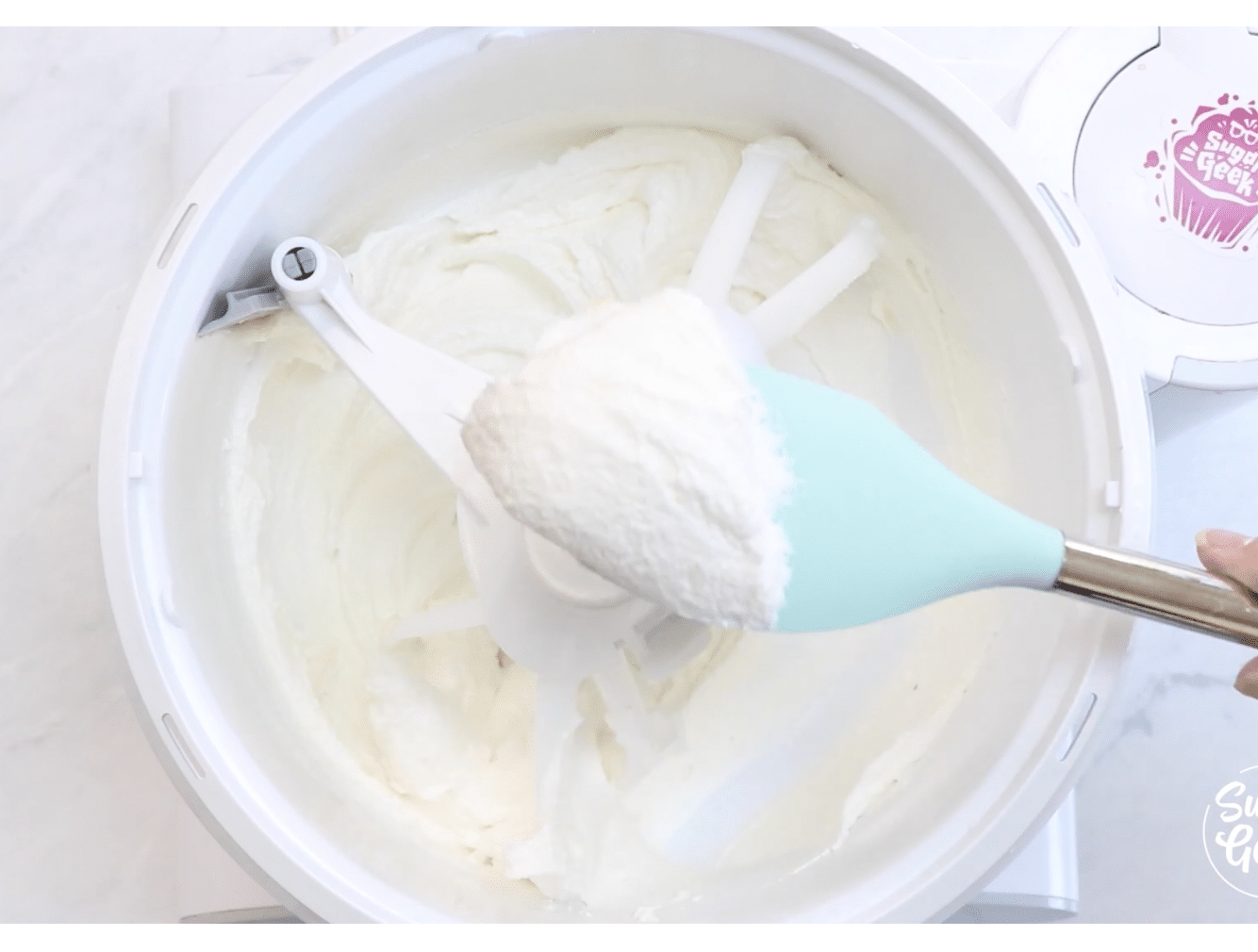 Whipped butter, sugar, and oil in a mixer with a rubber spatula showing the white, fluffy mixture on it.