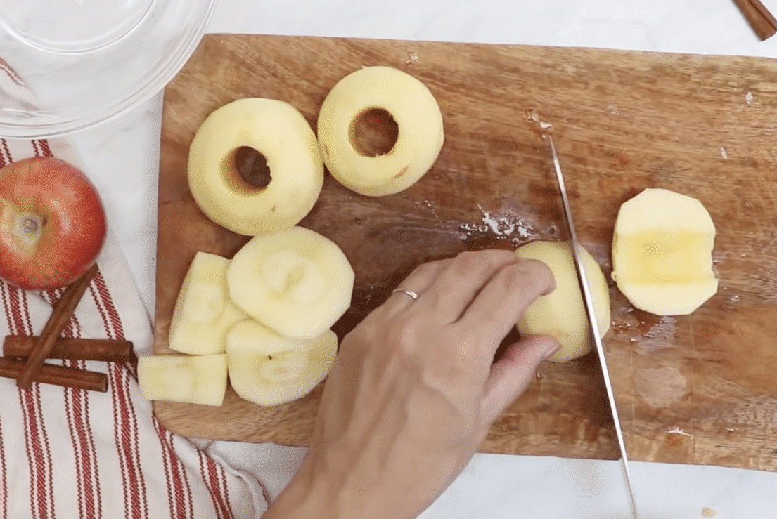 Peeled and cored apples being chopped on a wooden cutting board.