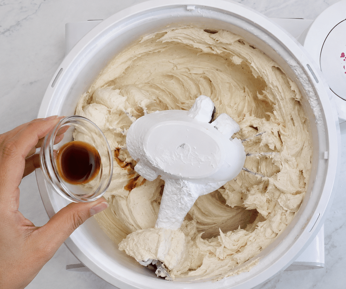 A hand adding vanilla extract to the brown butter frosting mixture.
