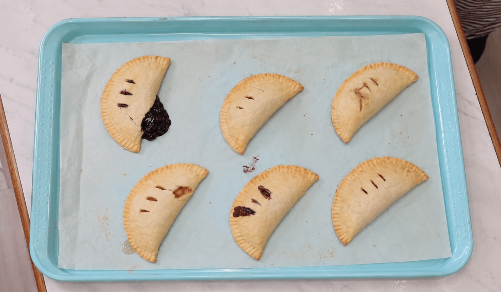 Six baked hand pies on a parchment-lined baking sheet.