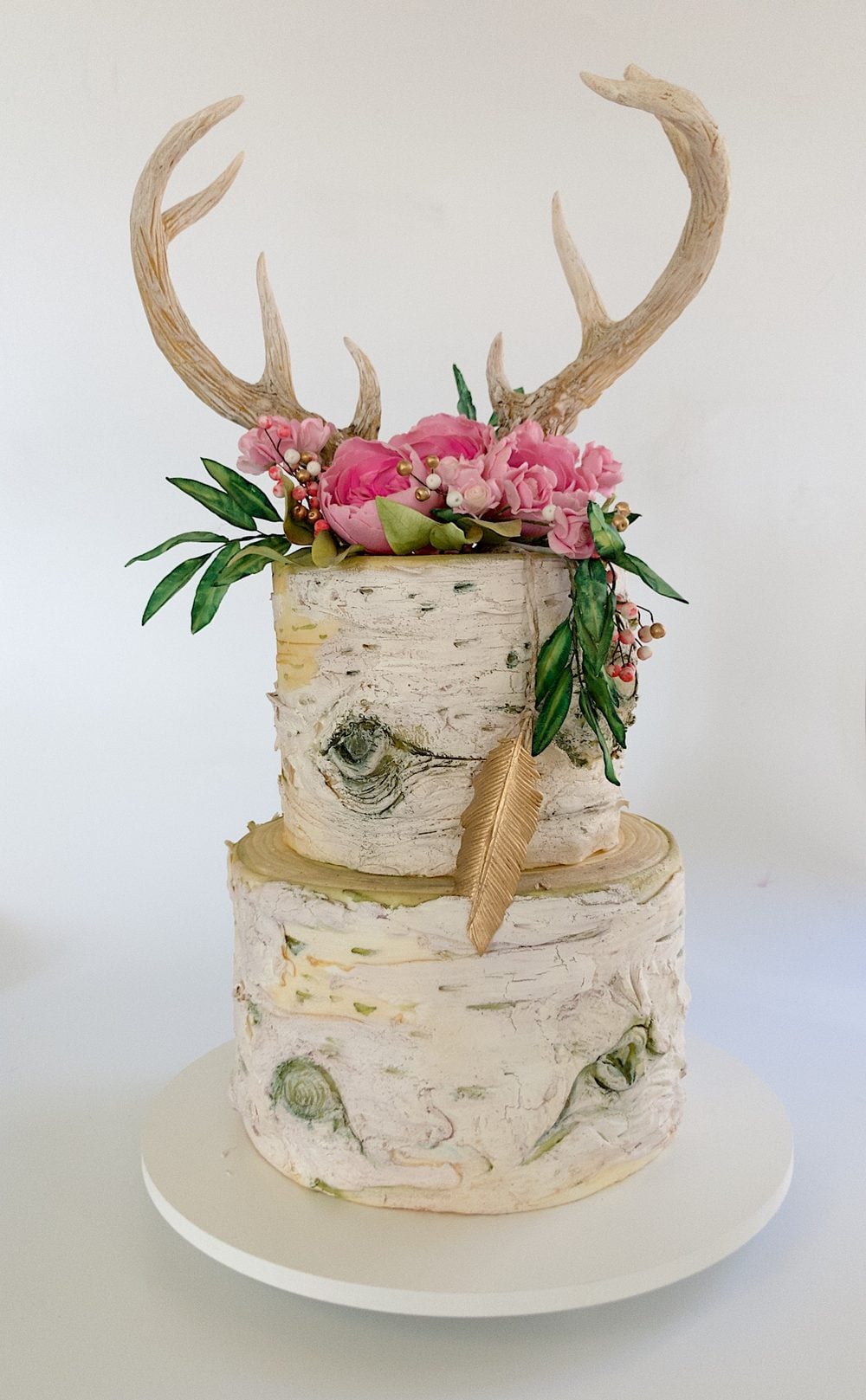 Two-tier birch bark bridal shower cake by Liz Marek topped with chocolate antlers, handmade sugar peonies, greenery, and a gold feather