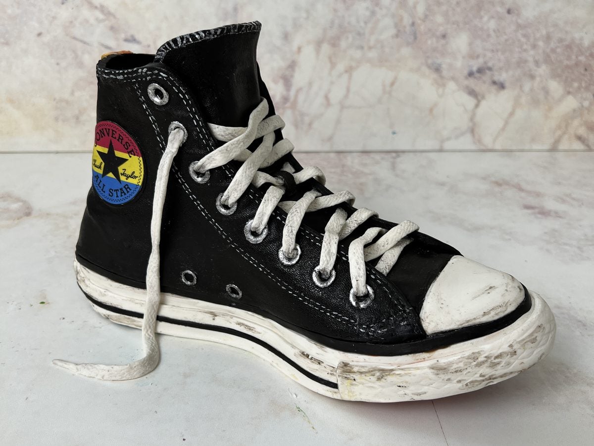 Hyperrealistic cake sculpted to look like a scuffed black high-top sneaker with white laces, by Liz Marek