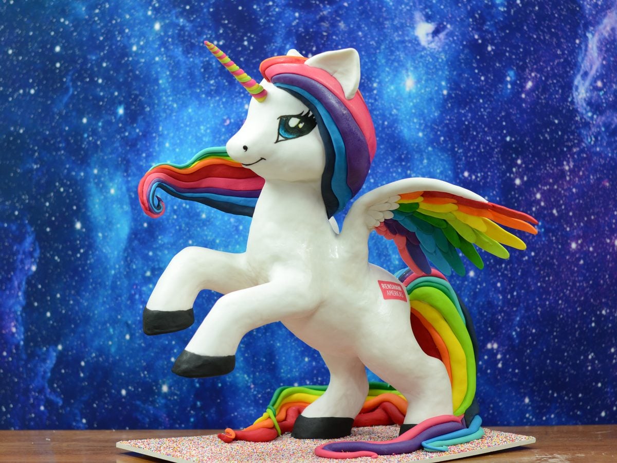 Large sculpted rainbow unicorn showpiece cake by Liz Marek, rearing up with rainbow mane, tail, and wings against a galaxy backdrop