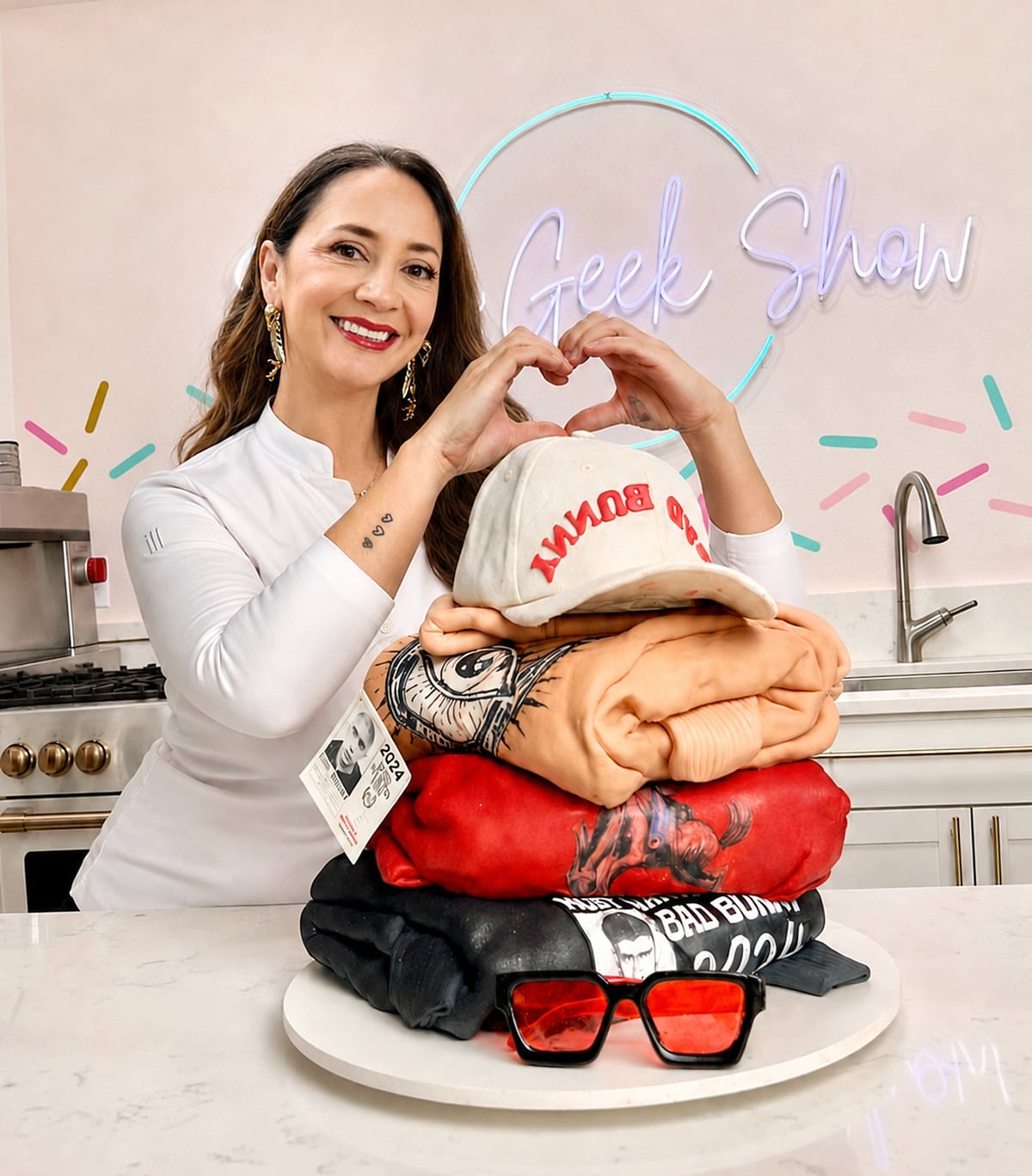 liz marek smiling, standing behind a sculpted cake in her studio holding up her hands in a heart shape