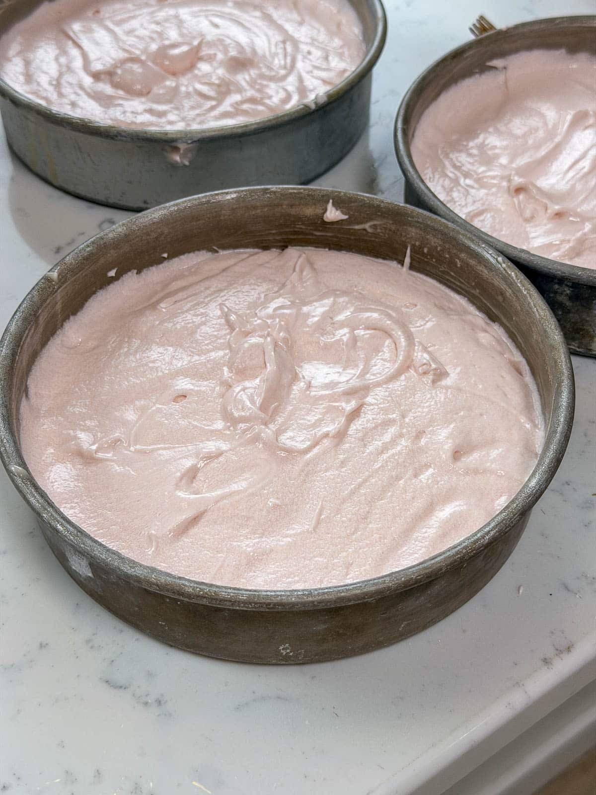 Pink champagne cake batter divided into three cake pans