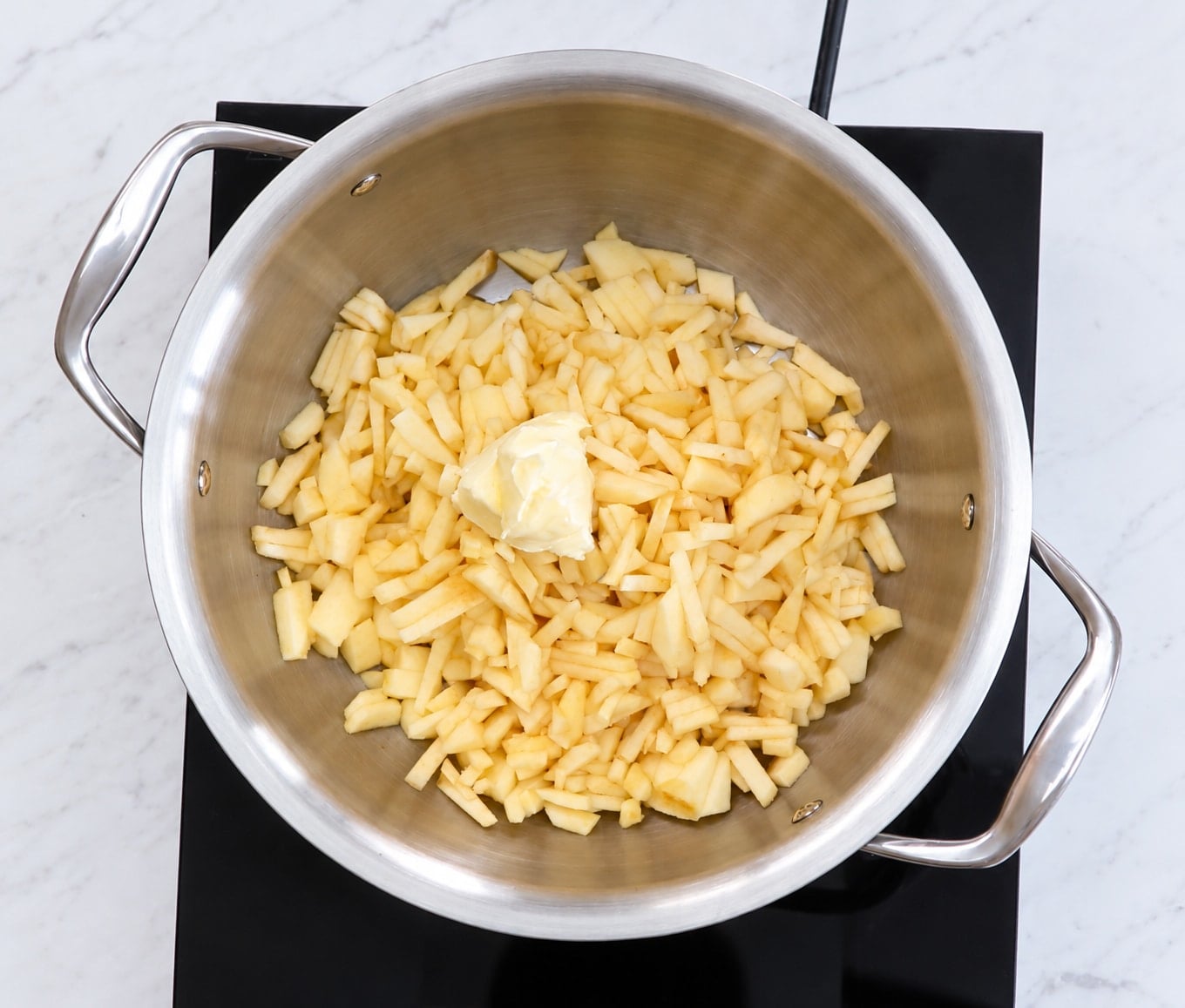 Chopped apples with a pat of butter in a stainless steel pan