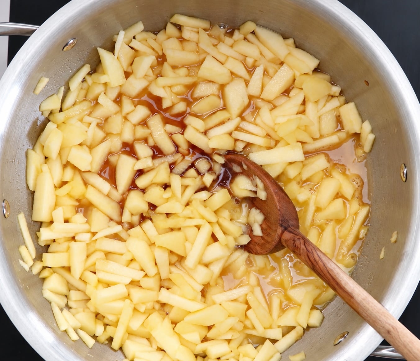 Stirring apple juice, brown sugar, and spices into chopped apples with a wooden spoon