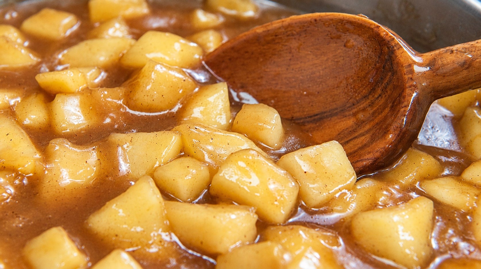 Close-up of thick, glossy apple pie filling with a wooden spoon