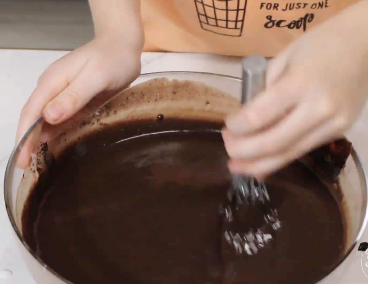 Whisking warm buttermilk into the black cocoa mixture in a glass bowl.