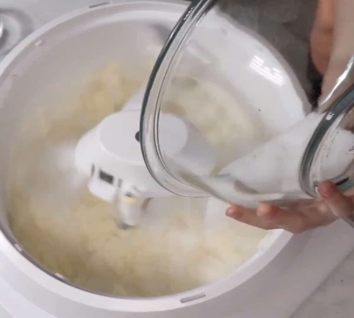 Pouring sugar into creamed butter in a stand mixer.