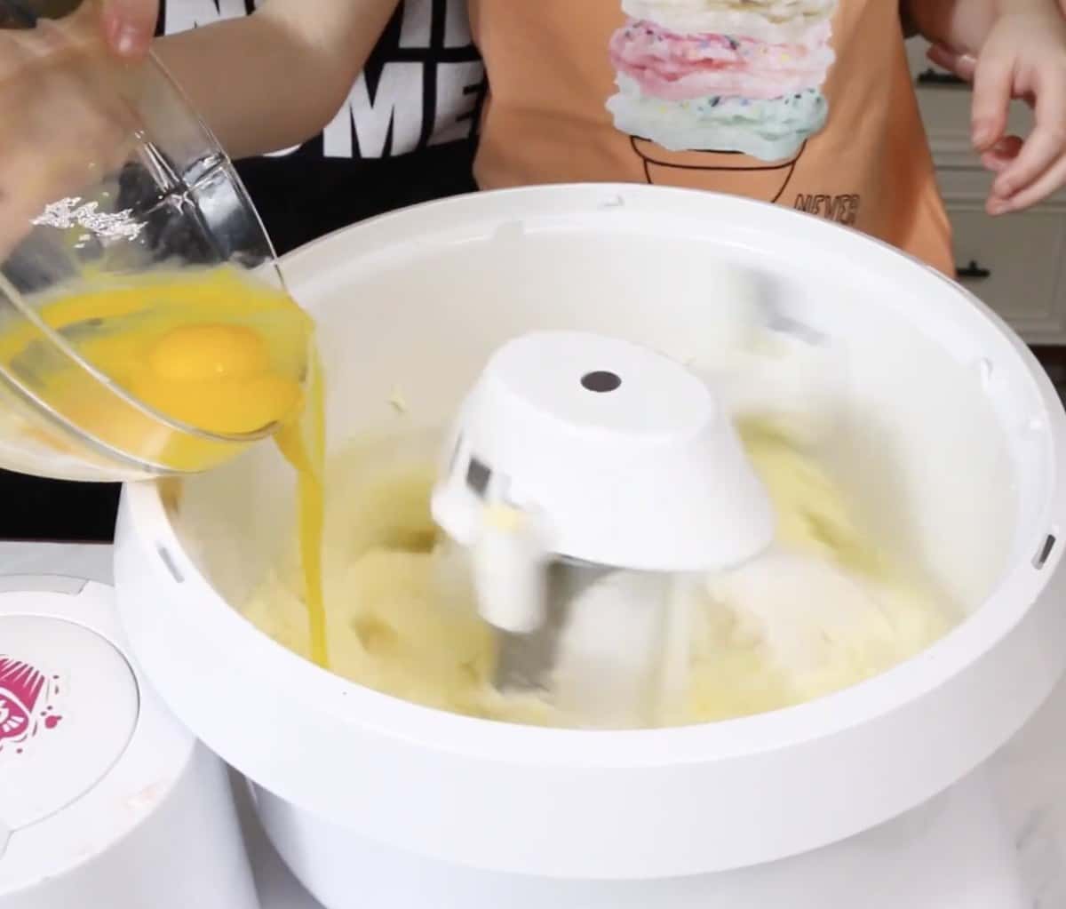 Adding an egg to creamed butter and sugar in a stand mixer.