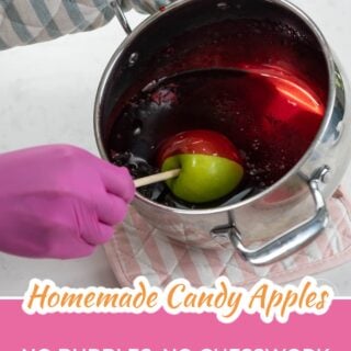 Green apple being dipped into hot red candy syrup in a stainless steel pot