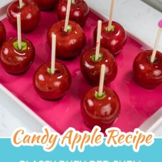 Red candy apples on wooden sticks lined up on a pink tray