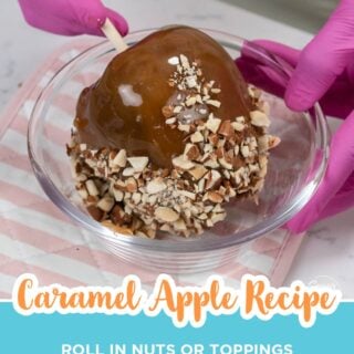 Caramel apple being rolled in chopped almonds in a glass bowl