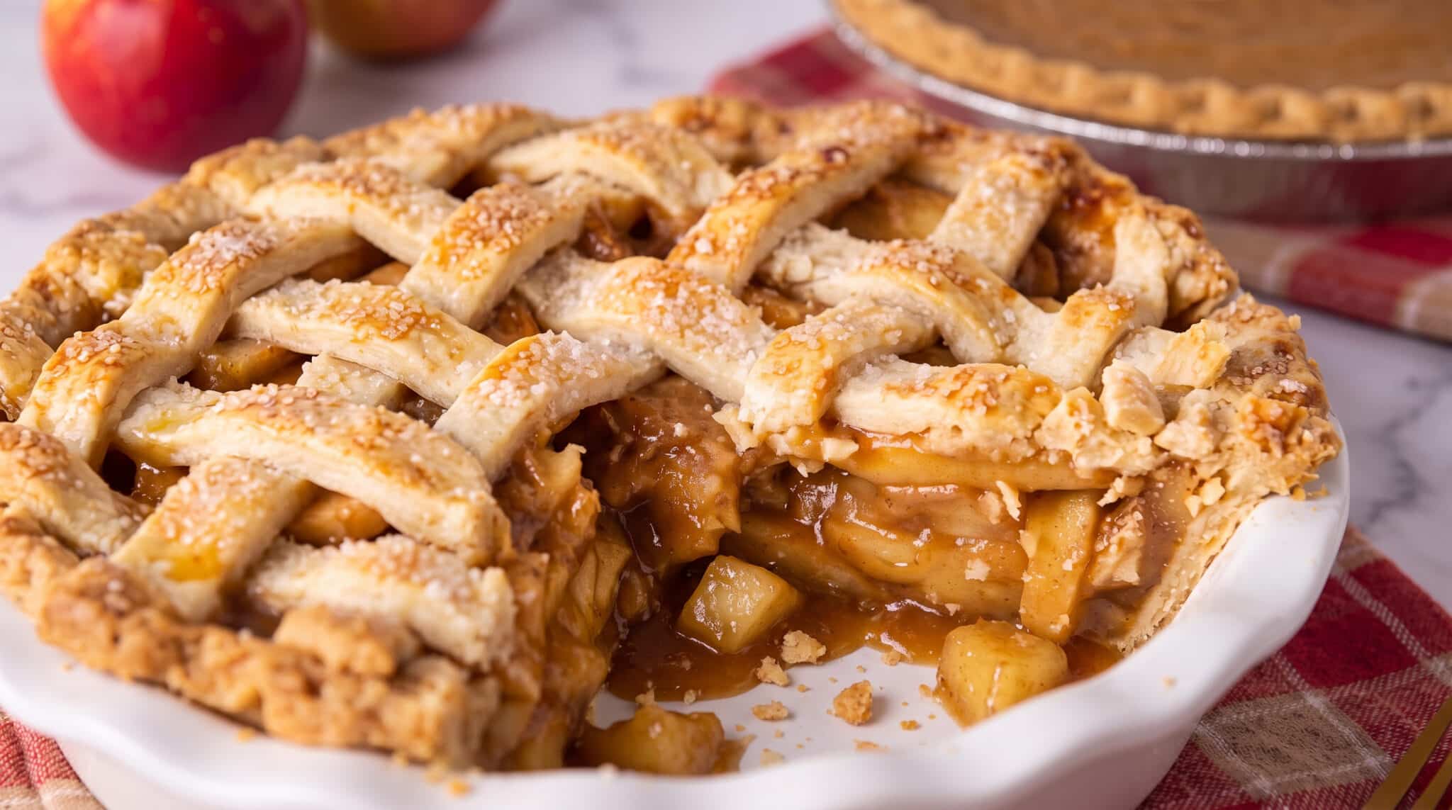 Caramel apple pie with a slice taken out of it in a white pie pan.