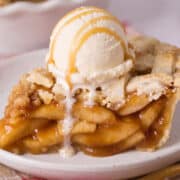 Close up of caramel apple pie slice with ice cream and drizzled caramel on top.