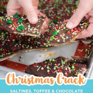 Hands breaking a sheet of Christmas crack topped with holiday sprinkles into pieces on a lined sheet pan.
