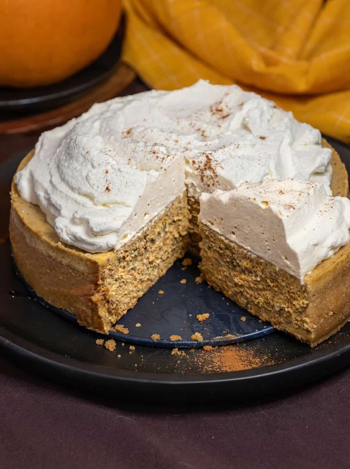A whole pumpkin cheesecake topped with whipped cream and pumpkin spice, with one slice cut and pulled out