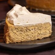 A slice of pumpkin cheesecake topped with whipped cream on a black plate
