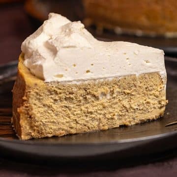 A slice of pumpkin cheesecake topped with whipped cream on a black plate