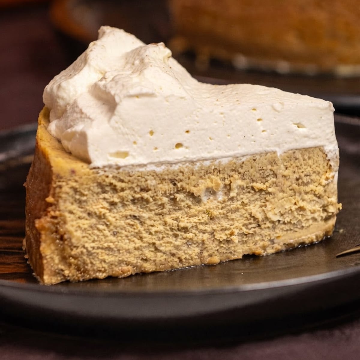 A slice of pumpkin cheesecake topped with whipped cream on a black plate