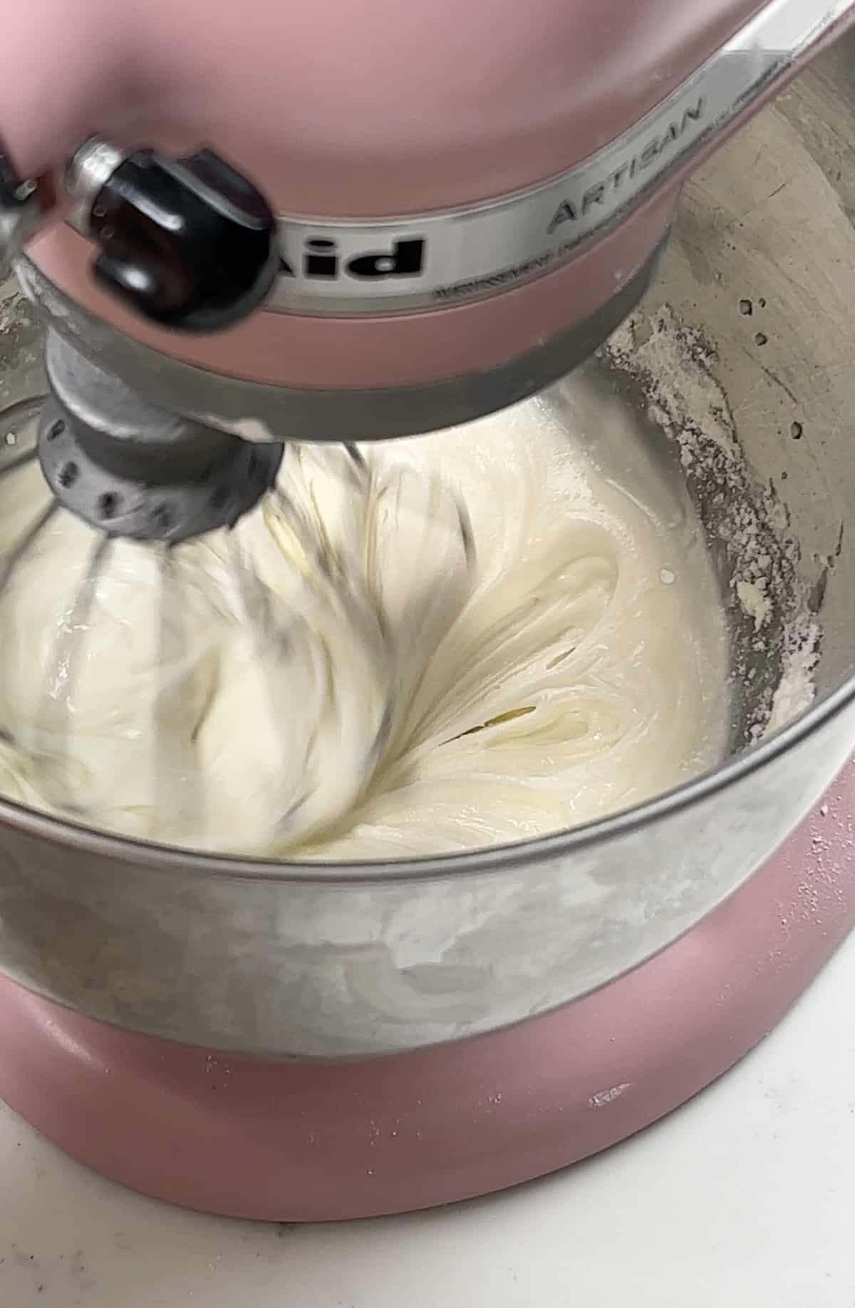 Royal icing being whisked in a pink KitchenAid stand mixer.