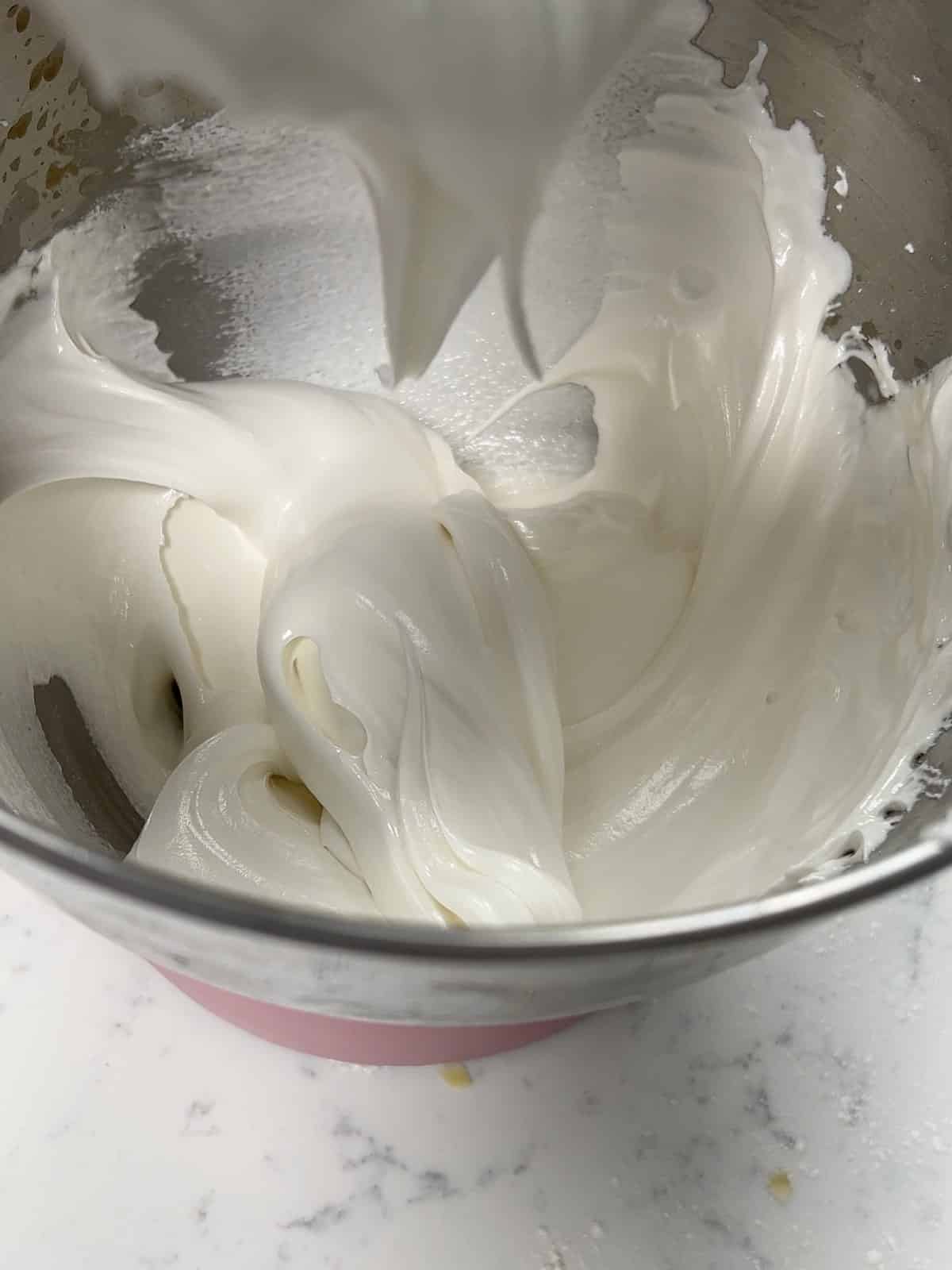 Thick, glossy royal icing holding stiff peaks in a mixer bowl.