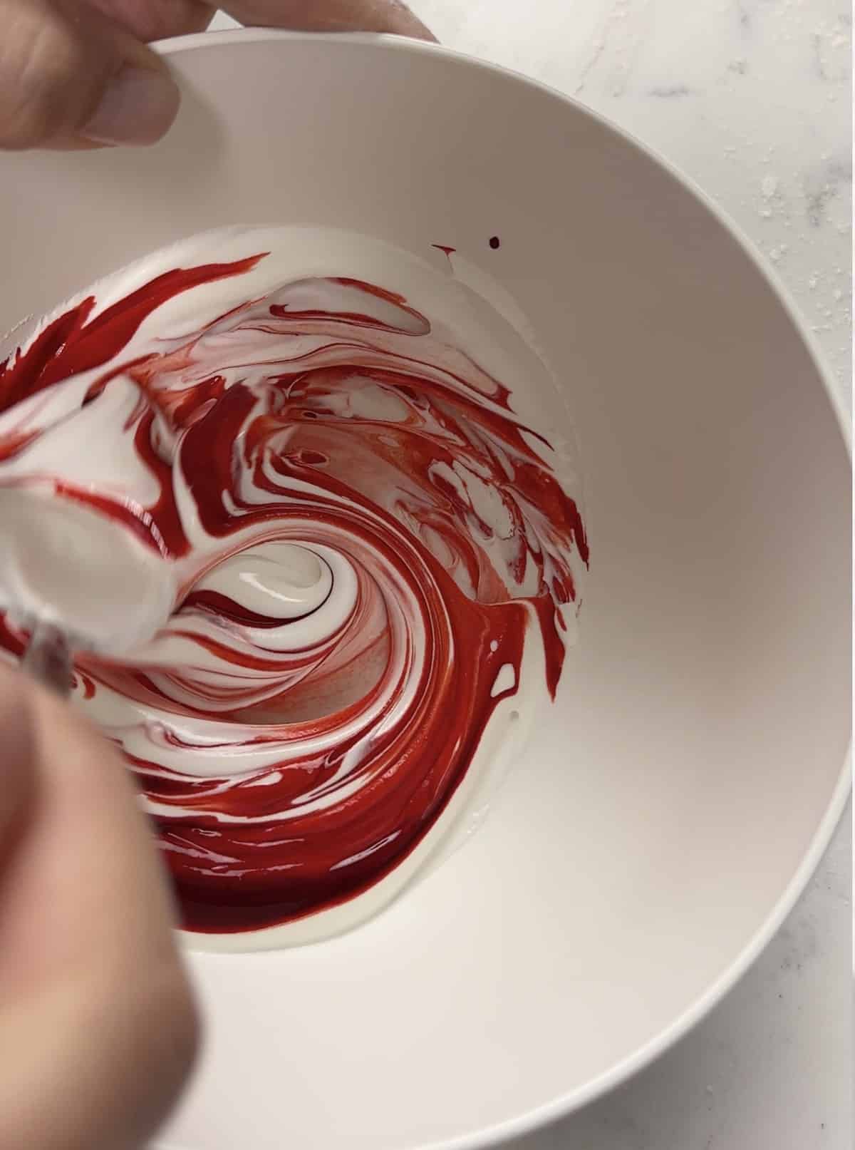 Red gel food coloring being stirred into white royal icing.
