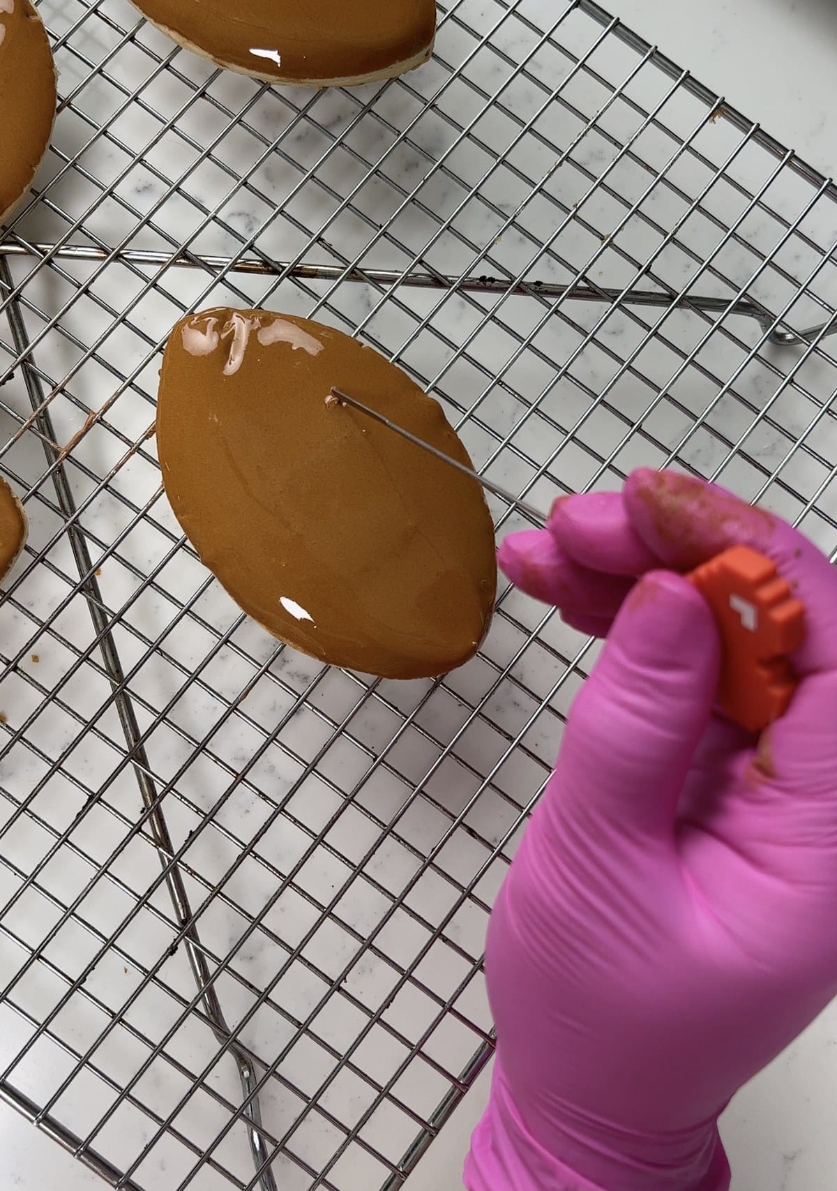 Smoothing royal icing on a dipped football cookie with a scribe tool.