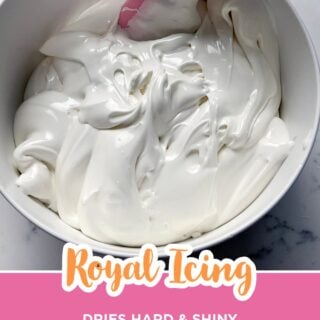 Bowl of thick, glossy white royal icing with a pink spatula.