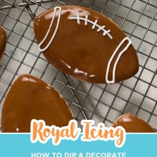 Football sugar cookies dipped in glossy brown royal icing with piped white laces on a cooling rack.