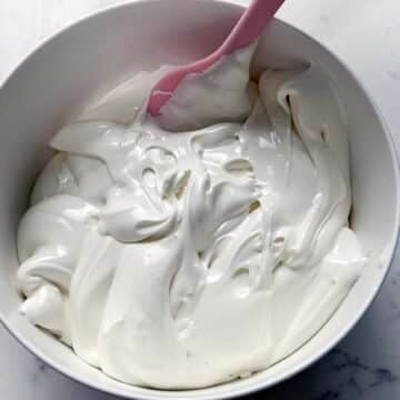 Bowl of thick, glossy white royal icing with a pink spatula.
