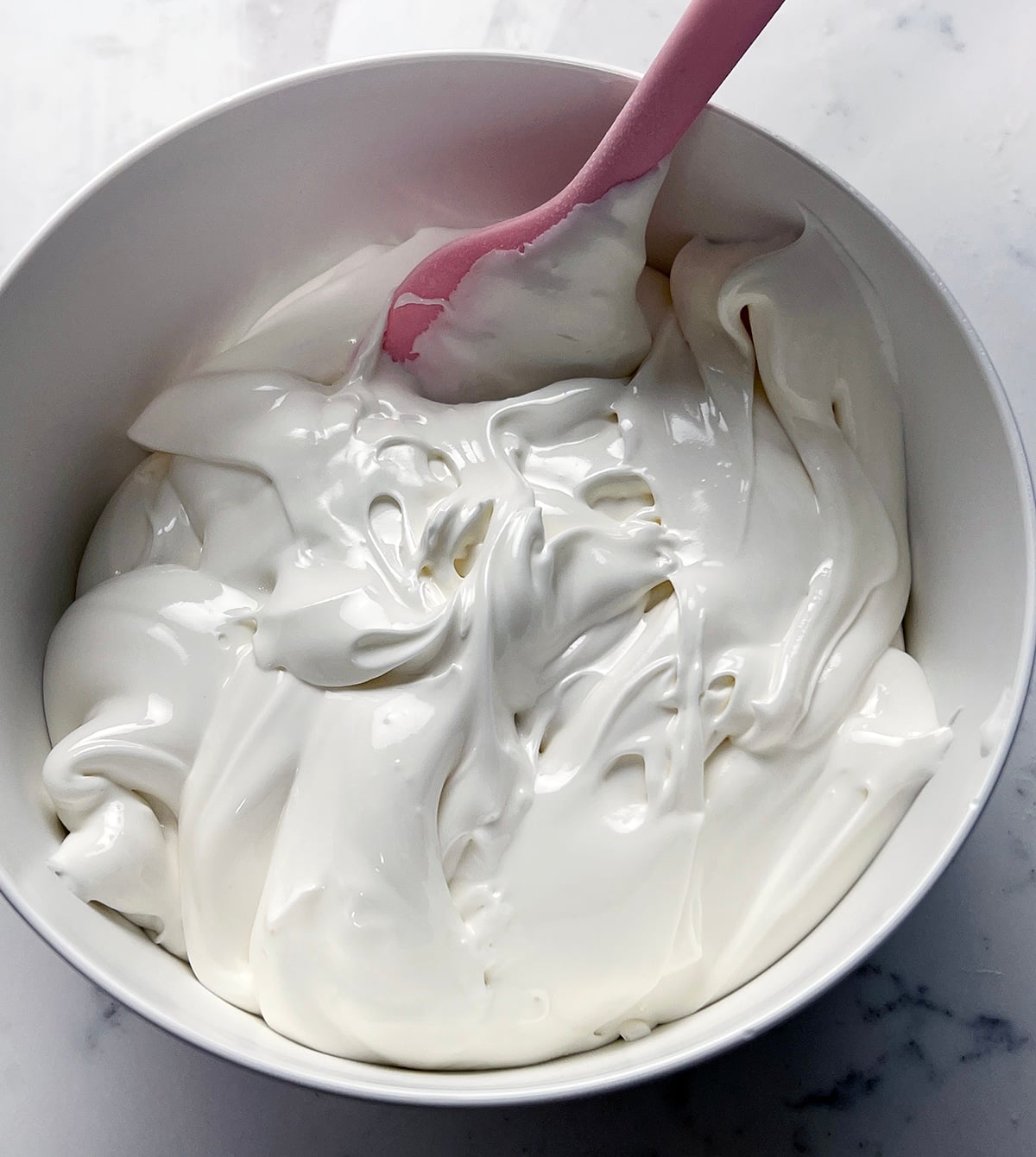 Bowl of thick, glossy white royal icing with a pink spatula.