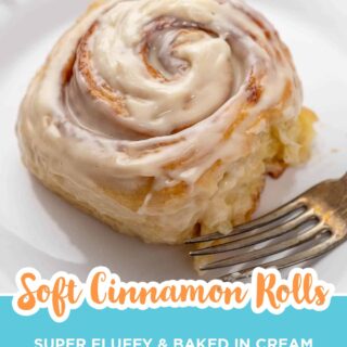 Soft cinnamon roll with cream cheese frosting on a white plate with a fork